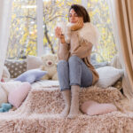 Retrato Caloroso De Mulher Sentada No Parapeito Da Janela Com Uma Xicara De Cha Quente Cafe Sueter E Lenco Branco 150x150